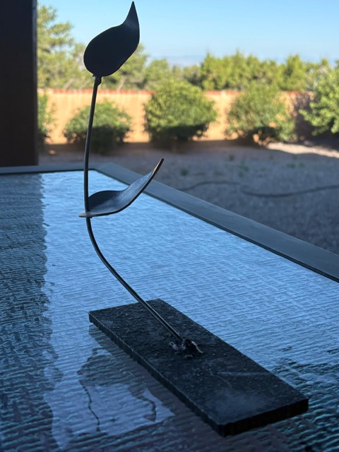 A slender black steel sculpture with two abstract leaf forms balanced along a curved stem on a rectangular base.